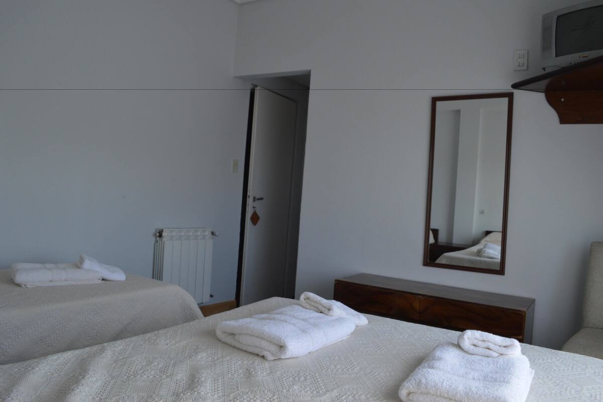 A hotel room with two beds, a wooden dresser, a mirror, and a radiator.