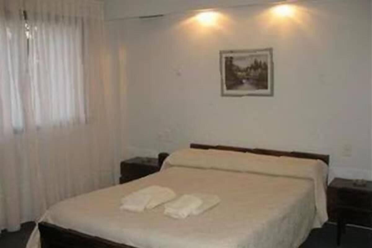 A single bed with a white bedspread and two pillows, a nightstand to the right, and a framed picture on the wall.