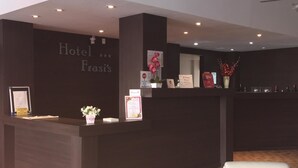 A hotel reception area with a dark reception desk, a white chair, and a carpeted floor.