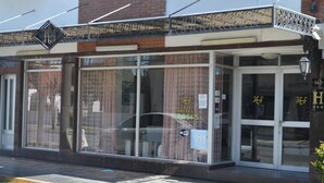 A hotel facade with large windows, a metal awning, and a sign indicating the name and address.