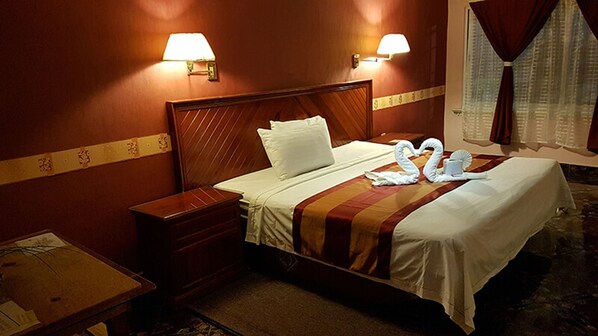 A hotel room with a wooden headboard, a bed with white linens, two wall-mounted lamps, and a window with curtains.