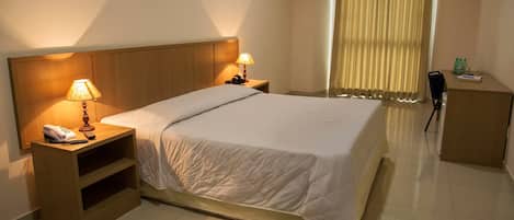 Ein Hotelzimmer mit einem Bett, Nachttischlampen, einem Schreibtisch mit Stuhl und einem fenster mit Vorhängen.