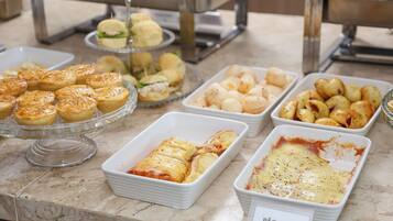 Un bufé con diversas opciones de panadería, incluyendo pasteles, pan y un plato etiquetado como 'Pão Pizza'.