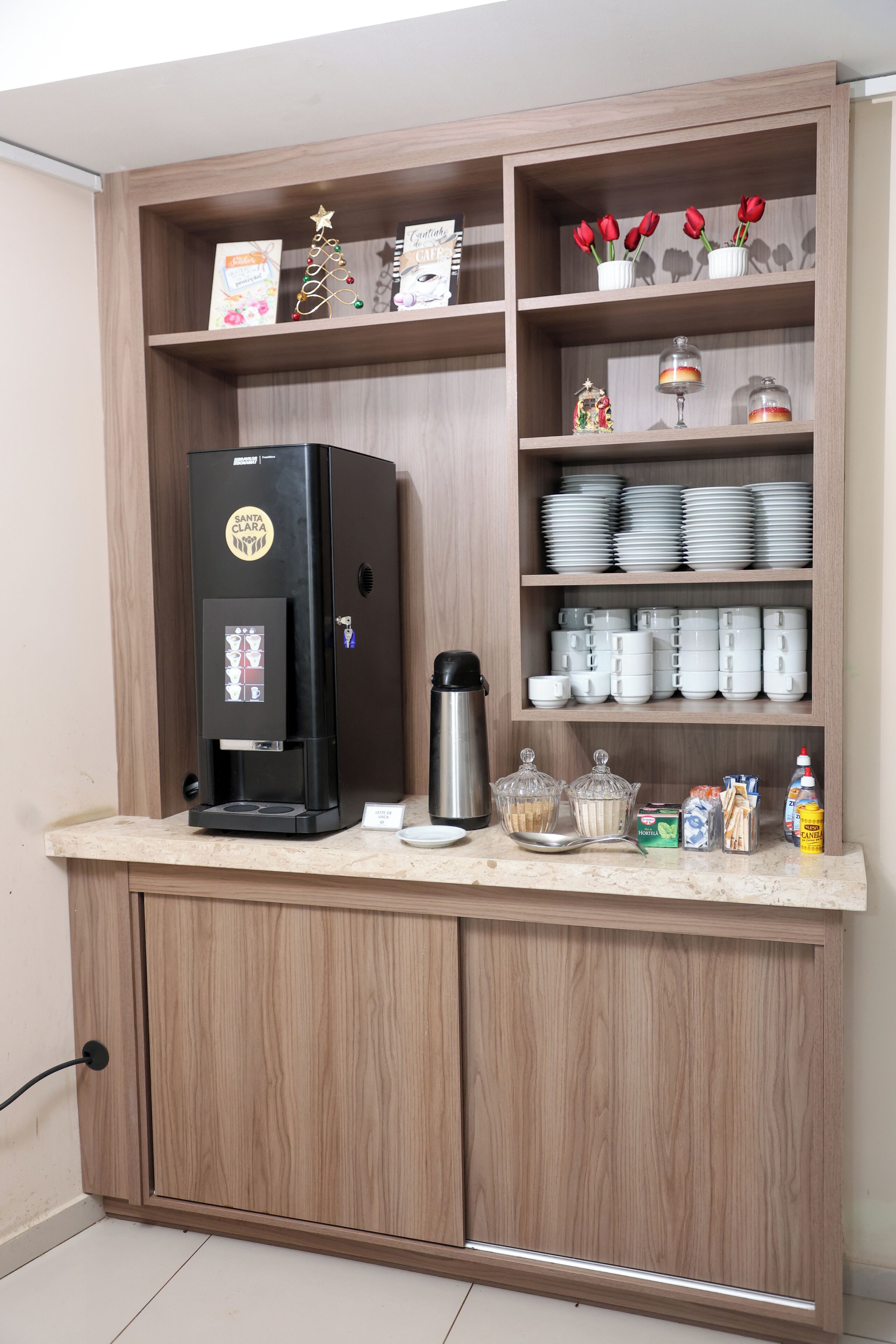 Una kitchenette con cafetera, repisas con platos y tazas, y un pequeño árbol de Navidad.