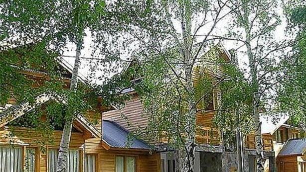 Una hilera de cabañas de madera con cimientos de piedra, rodeadas de árboles y un césped bien cuidado.