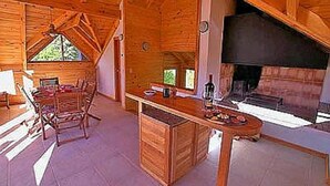 Interior de una cabaña de madera con comedor, chimenea y un ventanal grande.