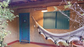 A hammock tied between a rustic building with a blue door and a window, and a tree in the foreground. - Pousada Casa de Taipa (São Miguel do Gostoso)