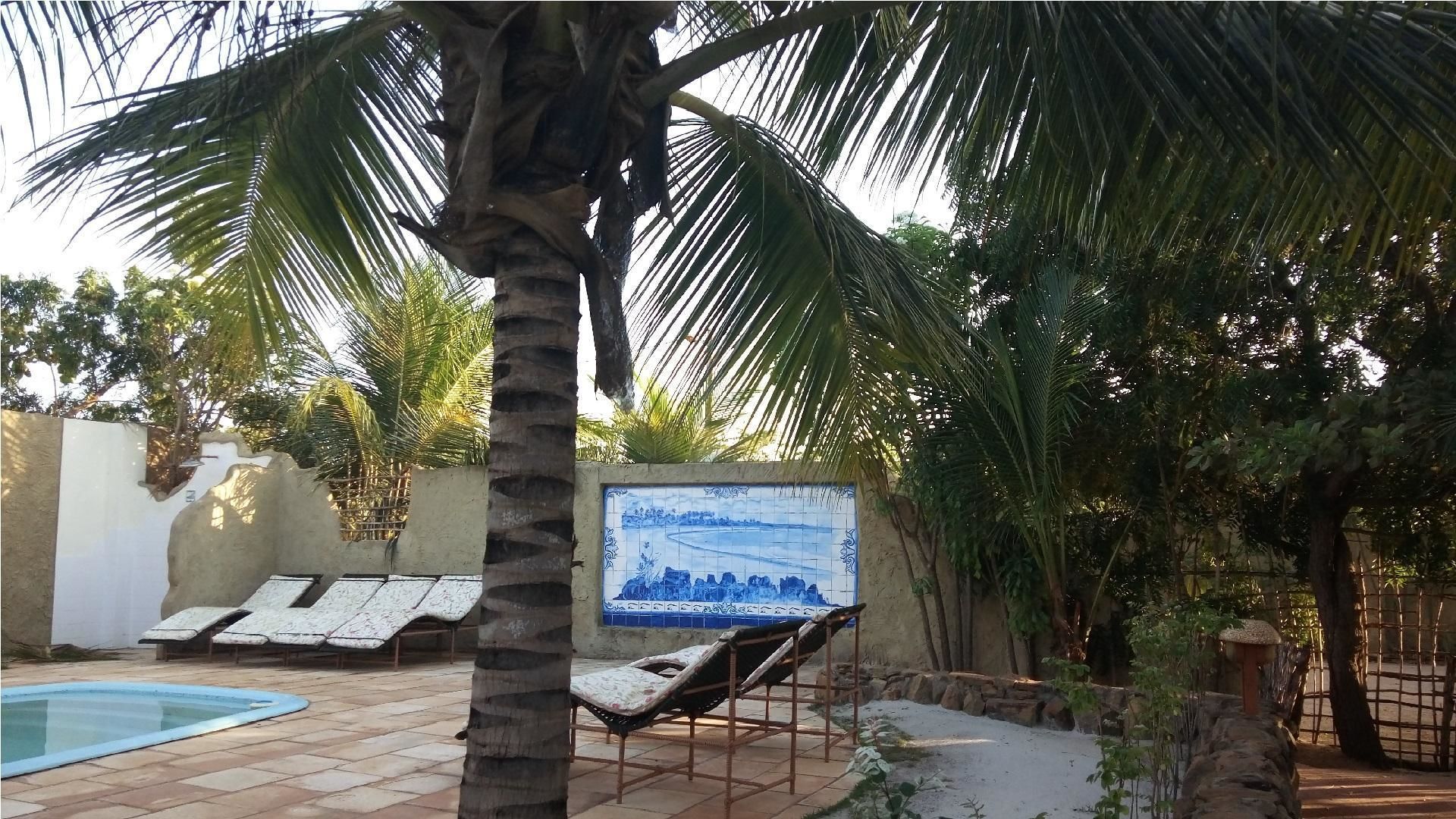 A pool area with lounge chairs, a tiled wall with a blue mural, and palm trees.