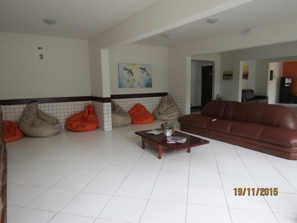 A living room with a brown leather sofa, orange bean bags, a wooden coffee table, and a tiled floor. - Água Doce Praia Hotel (Ubatuba)