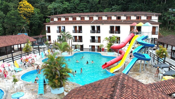 A resort with multiple swimming pools, a water slide, and a building with balconies. - Água Doce Praia Hotel (Ubatuba)