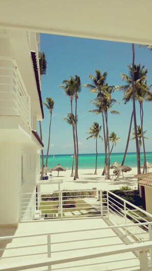 Ein Balkon mit Blick auf einen Strand, Palmen und einen wolkenlosen, blauen Himmel.