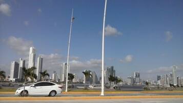 A cityscape with modern high-rise buildings, a white car on the road, and street lamps.
