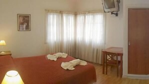 Una camera d'albergo con un letto, una scrivania, una sedia, un televisore a parete e un armadio.