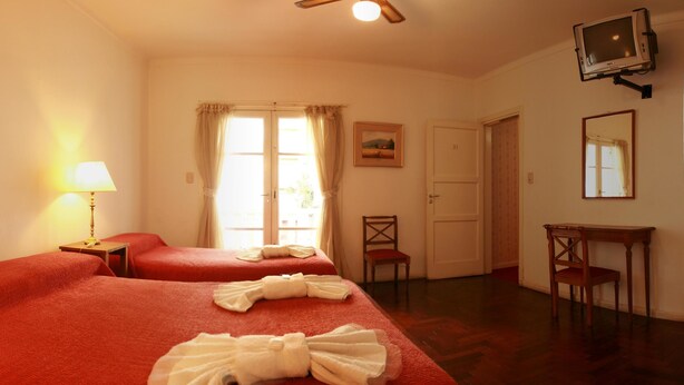Camera d'albergo con due letti, una scrivania, una sedia, una TV a muro e una porta.