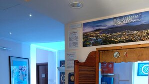A hotel lobby with a stone floor, wooden furniture, a reception desk, and a poster advertising a bed and breakfast in Naples. - B&B Il Golfo (Naples)
