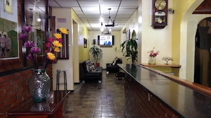 A hotel lobby with a reception desk, a TV screen, a clock, and a plant. - Hotel Europa (Bogota)