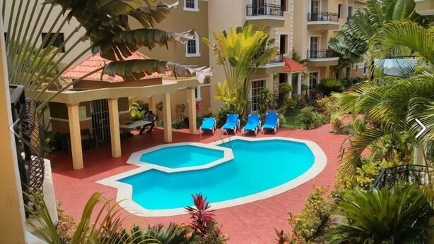 Zona de piscina con sillas de descanso y un edificio con balcones.