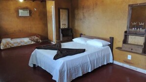 Una habitación con una cama individual, un banco de madera, un calentador en la pared y un espejo.