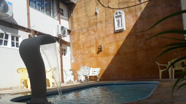 Una piscina con fuente, rodeada de mobiliario exterior y un edificio con pared texturizada.