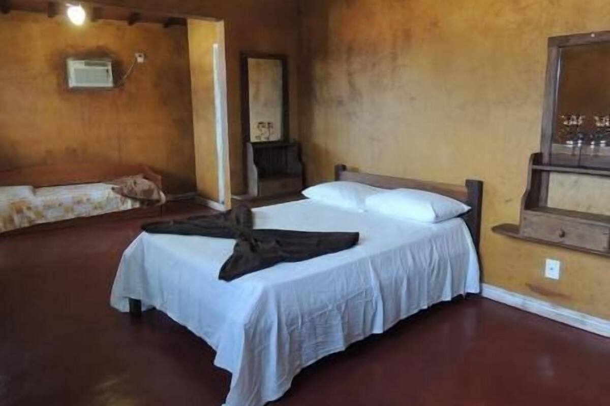 Une chambre avec un lit simple, une tête de lit en bois, une table de chevet et un climatiseur fixé au mur.