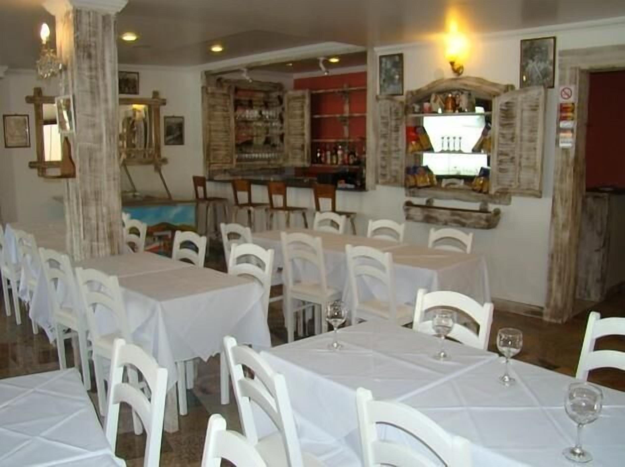 A restaurant with white tables and chairs, a bar area, and a chandelier.