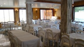 Un comedor amplio e interior con varias mesas y sillas, ventanas grandes y un candelabro.
