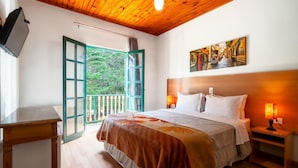 A bedroom with a wooden ceiling, a bed with a floral bedspread, a nightstand with a lamp, and a painting on the wall. - Castelo Piazzale by Concavus (Campos do Jordao)