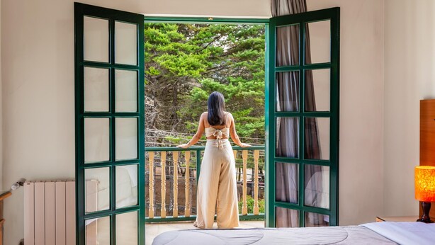 A room with a bed, a window with a view of trees, and a balcony with a railing. - Castelo Piazzale by Concavus (Campos do Jordao)