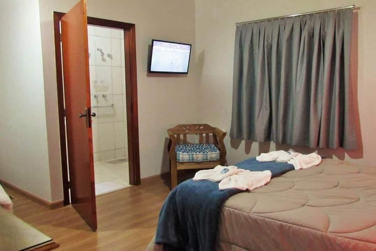 Un dormitorio con cama, una silla, televisión, ducha y cortina.