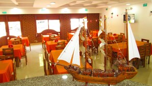 Un comedor con mesas y sillas, un modelo de barco sobre una encimera de granito y paredes de ladrillo.