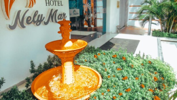 Entrada de hotel con una fuente, un letrero que dice "Hotel Nely Mar" y un jardín con flores de caléndula.
