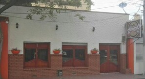 A building with three wooden doors and windows, each with a potted plant on the ledge.