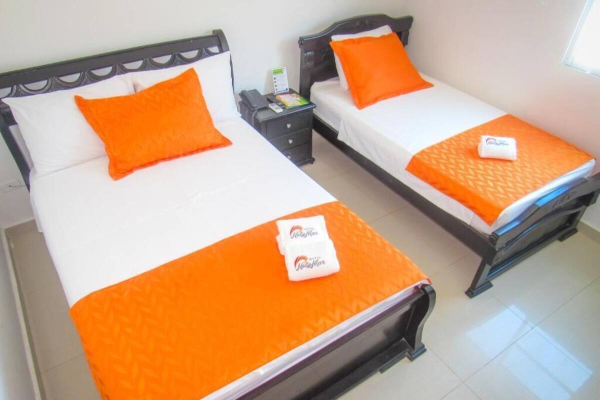 Deux lits jumeaux avec une literie orange et un oreiller blanc, une table de chevet avec un téléphone et une petite table, et une fenêtre avec des stores.
