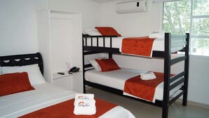Habitación con literas, paredes blancas, una ventana con vista a árboles y un armario blanco.