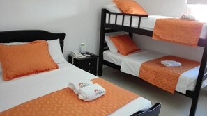 A hotel room with two beds, each with an orange bedspread and matching pillows. There is a black nightstand with a phone and a small table lamp.