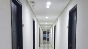 Un pasillo largo y estrecho con puertas negras a ambos lados y un suelo de baldosas brillantes.