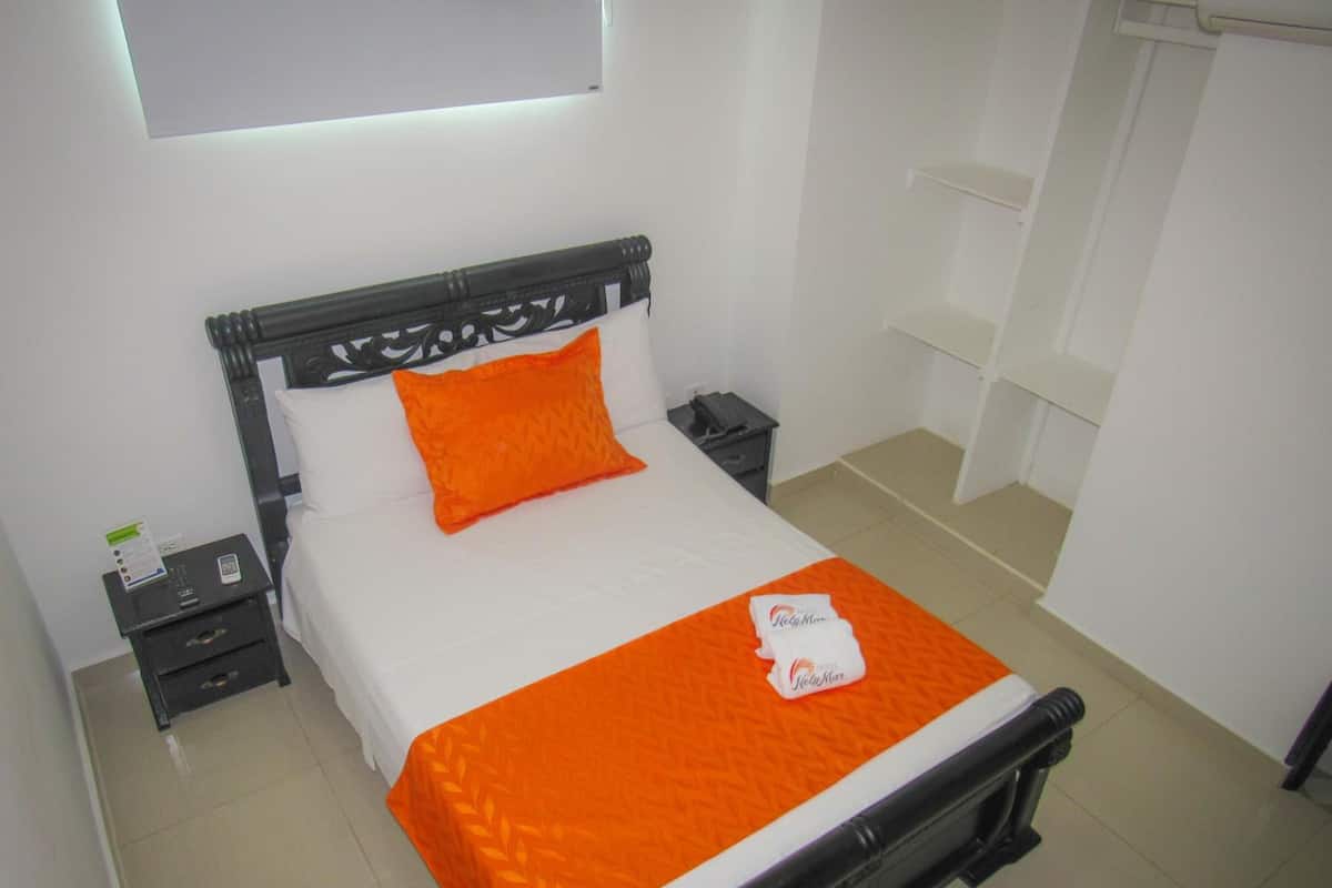 A neatly made bed with an orange bedspread and pillow, a black headboard, and a white wall with a window above it.