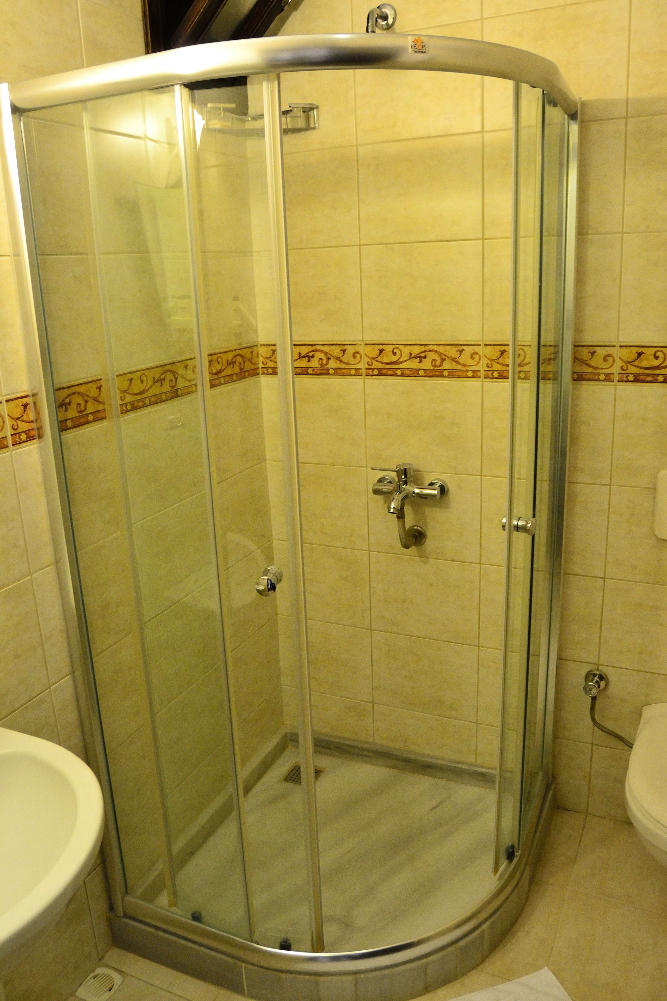 A glass-enclosed shower stall with a curved design, a wall-mounted faucet, and a tiled floor.