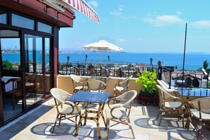 An outdoor seating area with wicker chairs and a glass table, overlooking a scenic view of the sea and city skyline. - Hotel Alp Guesthouse (Istanbul)