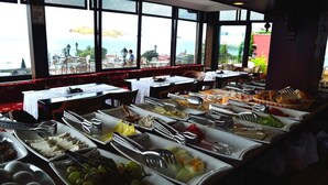 A buffet setup with various food items and utensils, tables with white tablecloths, and a view of the sea through large windows. - Hotel Alp Guesthouse (Istanbul)
