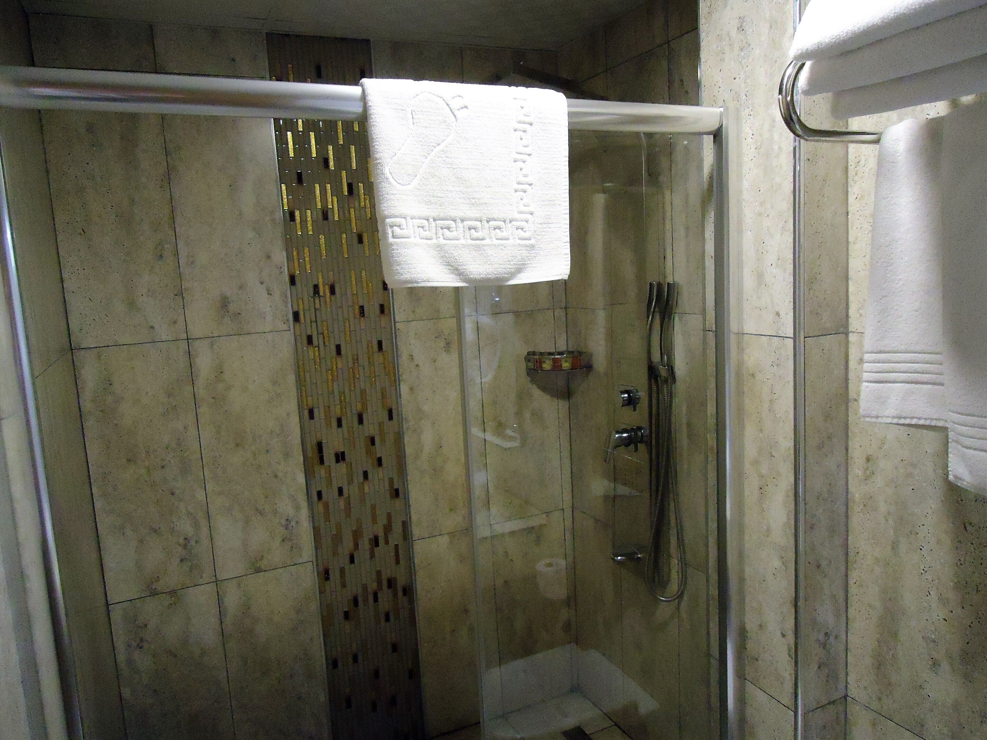 A glass-enclosed shower with a white towel hanging on the door, tiled walls, and a showerhead.