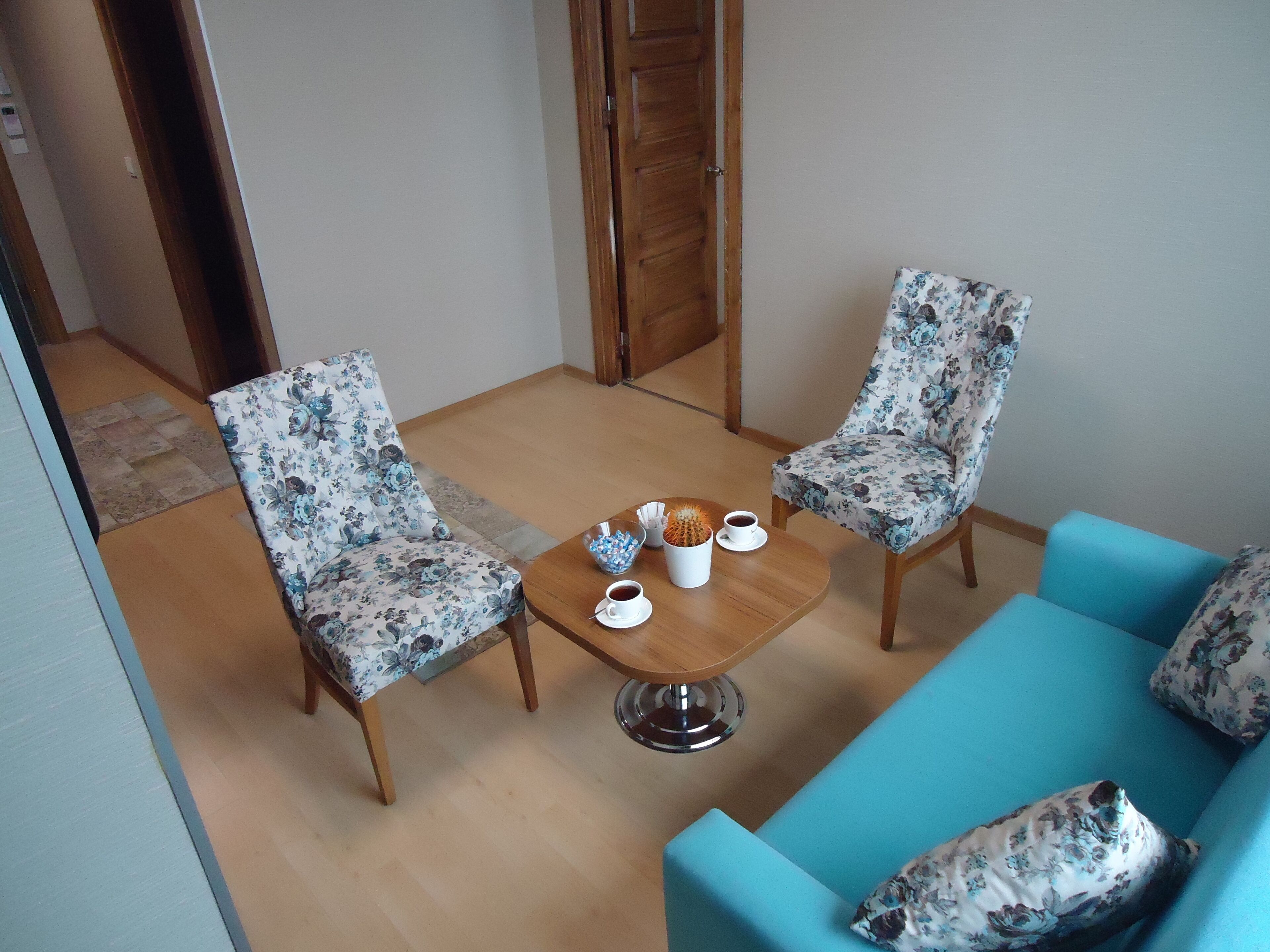 A room with two floral-patterned chairs, a wooden coffee table with cups and a cactus, and a blue sofa with floral cushions.