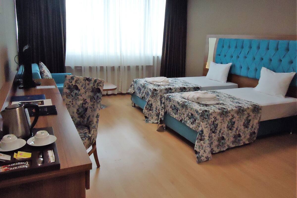 A hotel room with two beds, a desk, a chair, and a window with curtains.