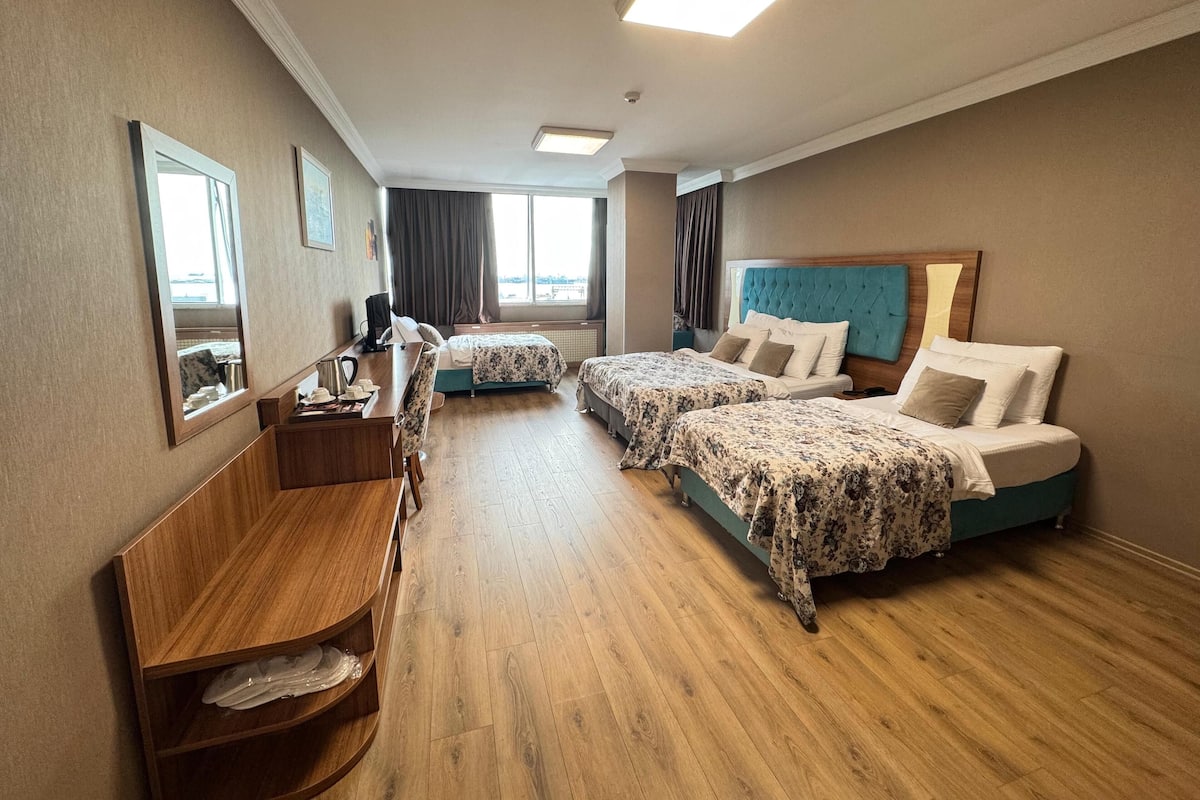 A hotel room with two beds, a desk, a chair, and a small shelf.