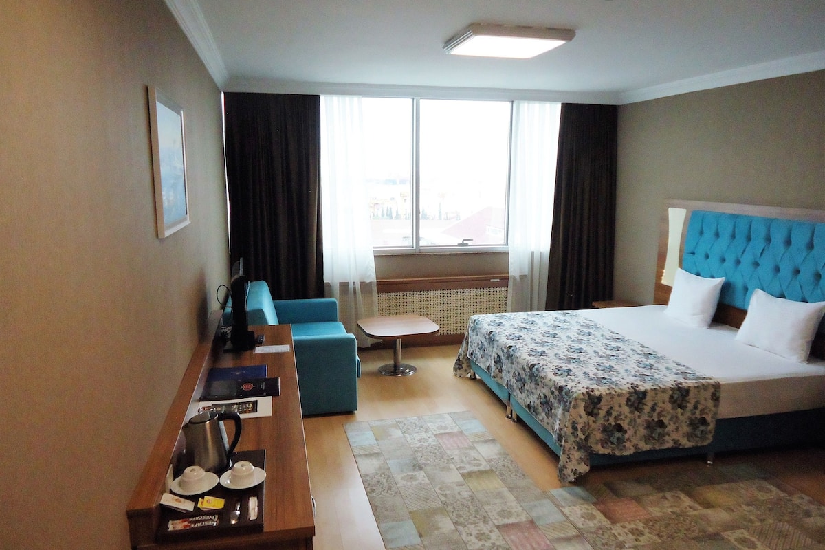 A hotel room with a bed, a desk, a chair, a small table, and a window with curtains.
