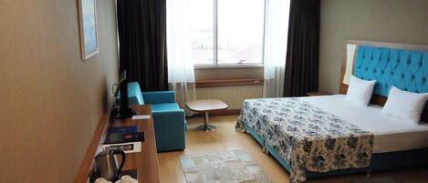 Ein Hotelzimmer mit Bett, Schreibtisch, Stuhl, einem kleinen Tisch und einem Fenster mit Vorhängen.