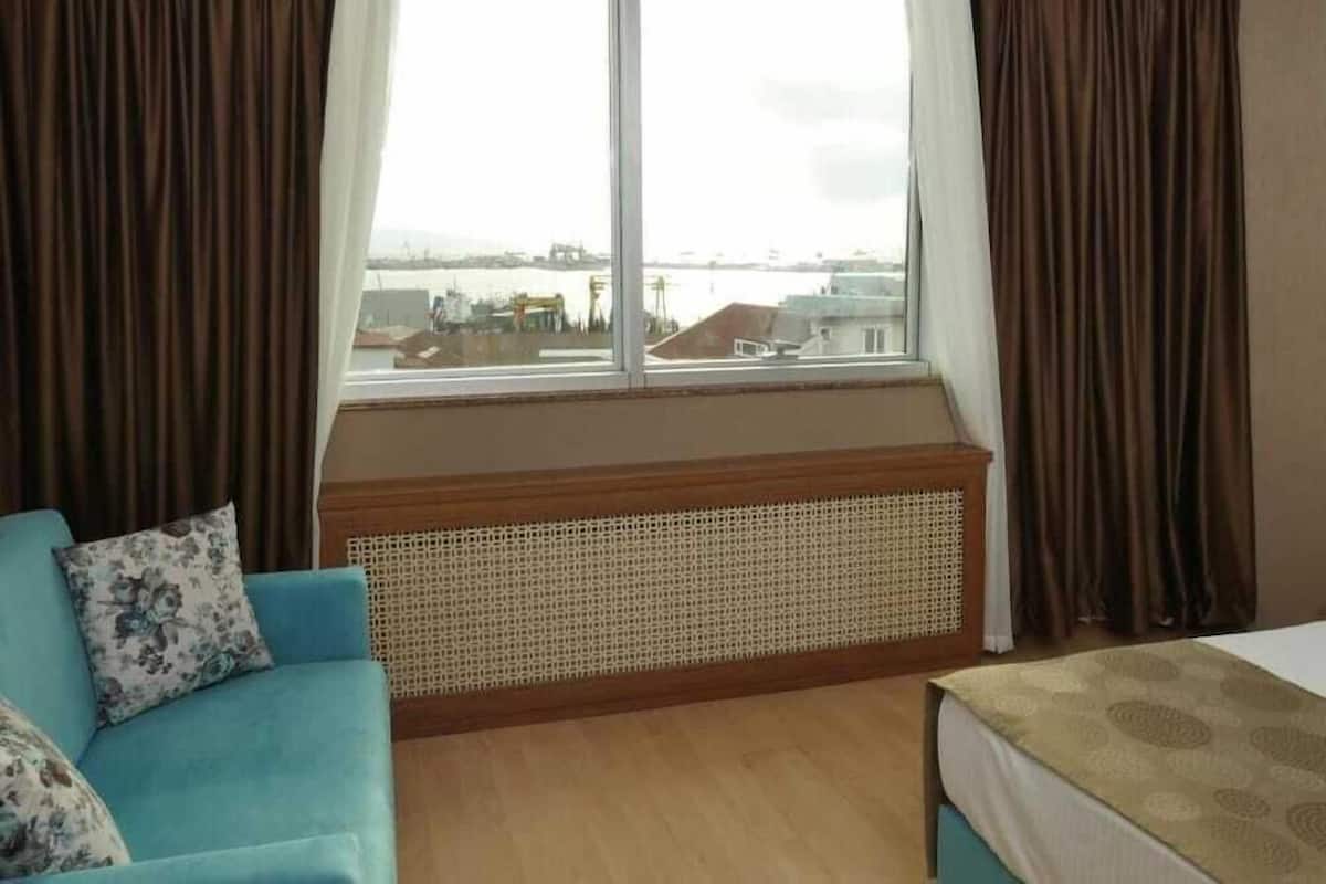 A hotel room with a large window, a sofa, a bed, and a rattan headboard.