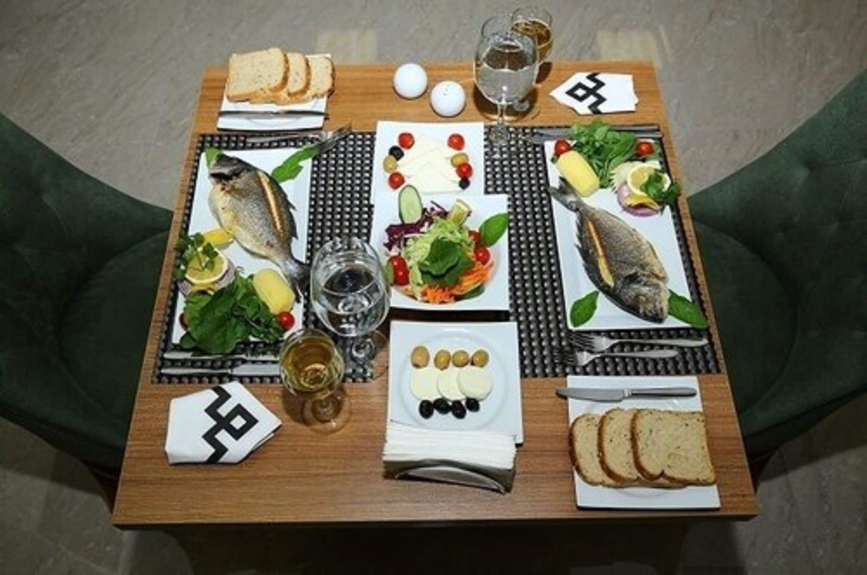A dining table set with various foods, including fish, vegetables, and bread, along with glasses and utensils.
