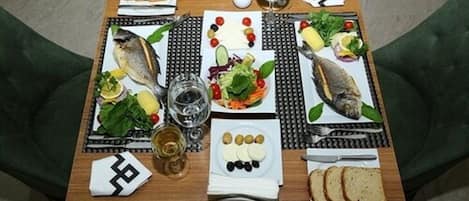 A dining table set with various foods, including fish, vegetables, and bread, along with glasses and utensils.