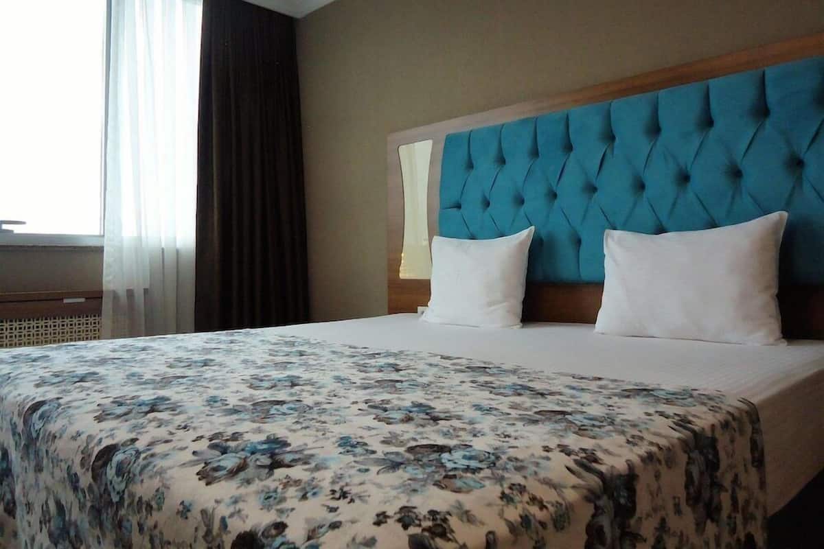 A hotel room with a large bed, a tufted headboard, and a window with curtains.